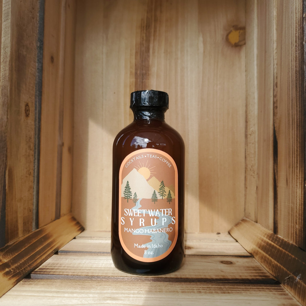 A bottle of Mango Habanero Syrup by Sweetwater Syrups sits in a rustic crate and is photographed from the front.