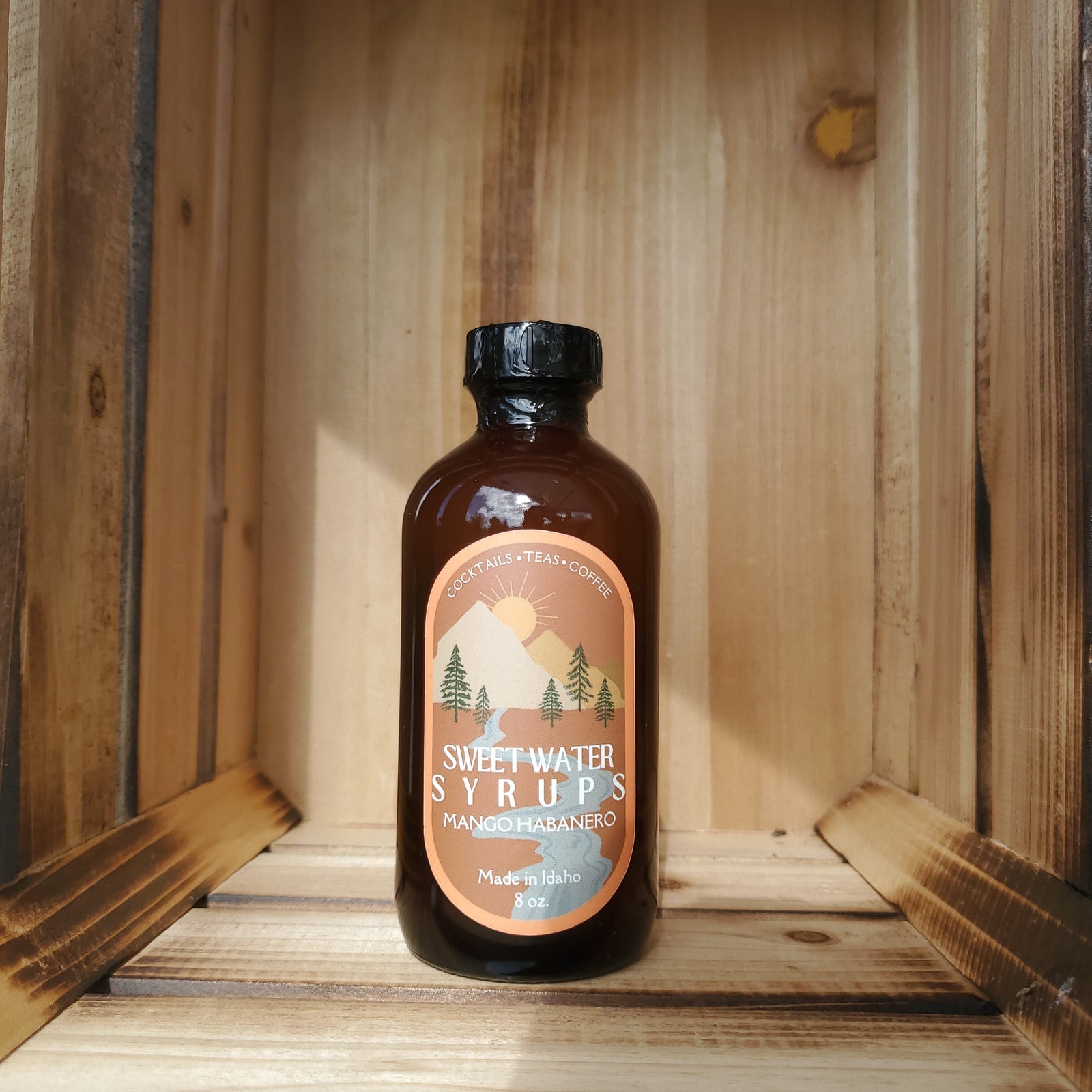 A bottle of Mango Habanero Syrup by Sweetwater Syrups sits in a rustic crate and is photographed from the front.